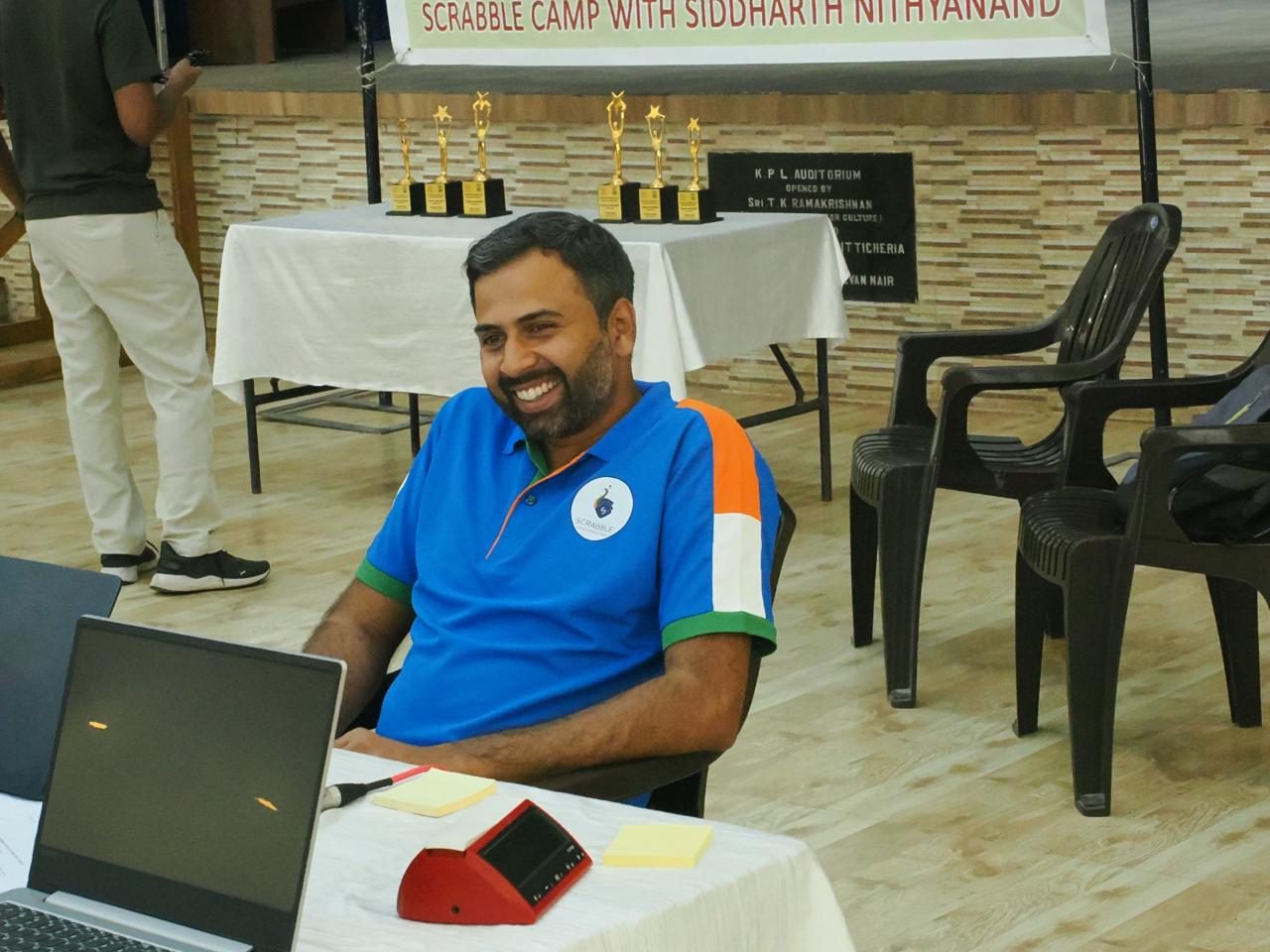 Sid at a Scrabble camp, seated beside the trophy table